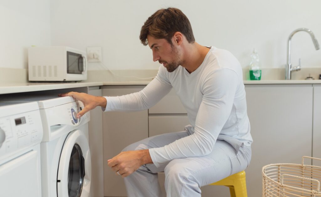 Side view of young Caucasian man cleaning clothes in washing machine at home
